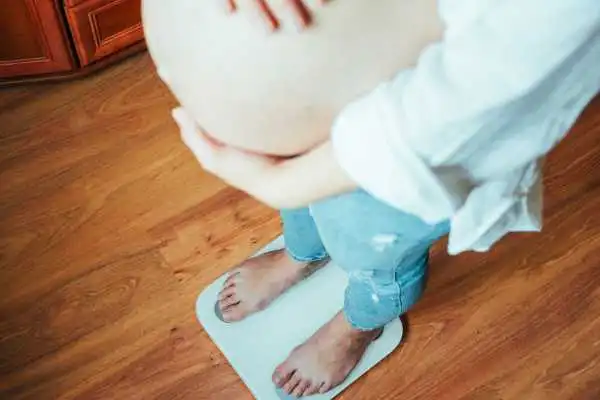 Image of woman weighing herself and experiencing weight gain through pregnancy Wakefield