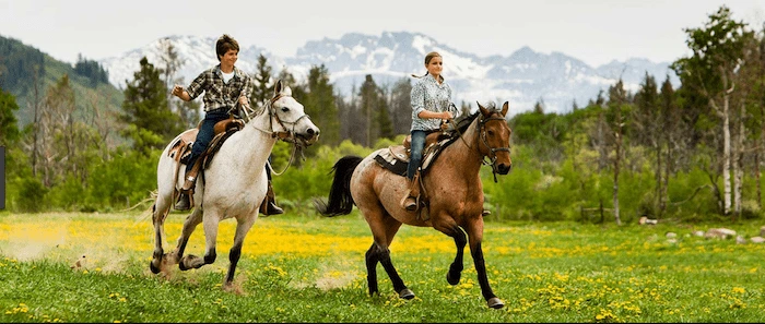 Confident plus-size woman riding Wakefield a horse through a field with a smile on her face.